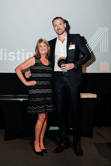 A smiling woman poses with a smiling man on stage after she presents an award to him on stage