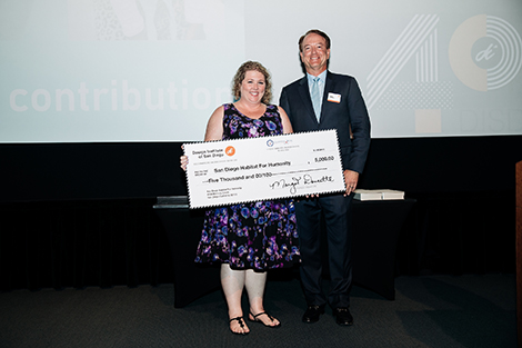 A smiling representative from San Diego Habitat for Humanity is on stage accepting a check for $5,000 from Design Institute of San Diego's CFO Dennis Doucette