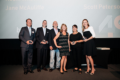Six board members from Design Institute of San Diego, three men and three women, are posing and smiling on stage during the awards ceremony